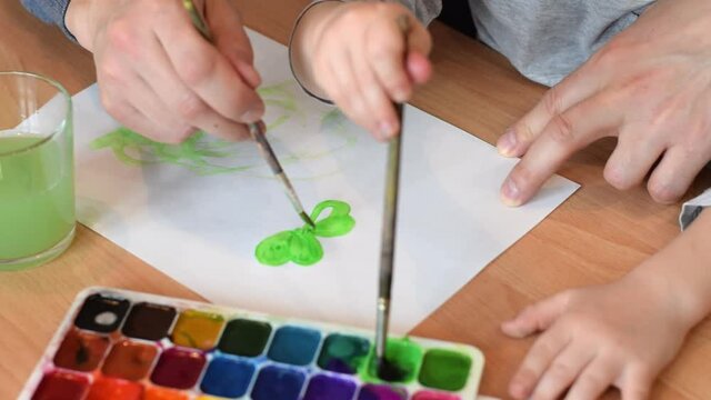 Dad and son paint a leaf of clover on a white sheet of paper with paintbrush and watercolors.Hands close up.Concept of St.Patrick's Day.Joint family leisure.