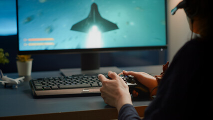 Closeup of competitive woman player holding joystick playing space shooter video games at powerful computer late night. Professional gamer using wireless controller for online gaming championship © DC Studio