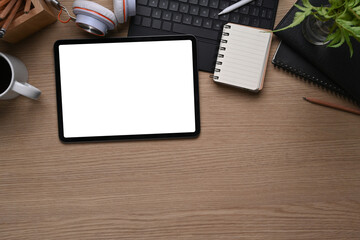 Top view of mock up digital tablet with whit screen, notebook, keyboard, headphone and copy space on wooden table.