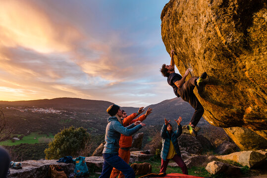 Man climbing granite boulder rock near friends