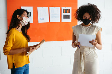 Diverse female colleagues in masks working with papers