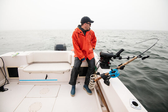 Man in raincoat on a boat with a fishing rod in the fog