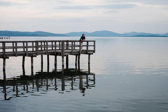 Man relaxing on a pier looking out at a calm lake.