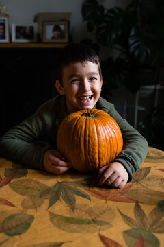 Laughing little boy with a pumpkin on a table