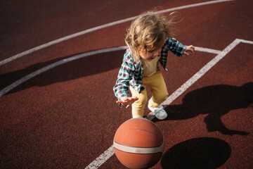 Little kid playing basketball ball on sports ground