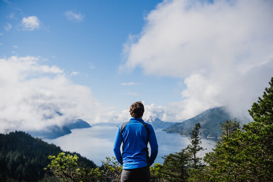 Man in blue fleece admires the sunny view of a rocky fjord.