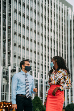 Stylish business colleagues in masks talking near urban building