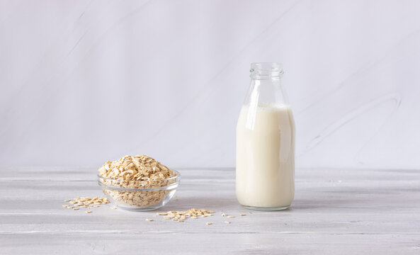 Vegetable Oat Milk In A Glass Bottle And Oat Flakes On A Light Background. Healthy Drinks, Vegetarianism. Side View