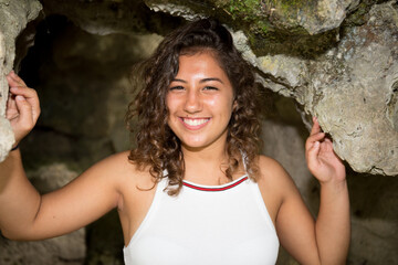 beautiful young woman smiling posing against nature rock background with curly hair and positive expression