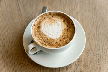 Cup of freshly brewed Cappuccino with latte art foam on a table of the cafeteria