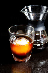 Cold americano decoration with ice ball in whisky glass on a black table.