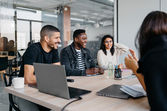 Group of multiracial businesspeople laughing and smiling during a meeting in modern workplace