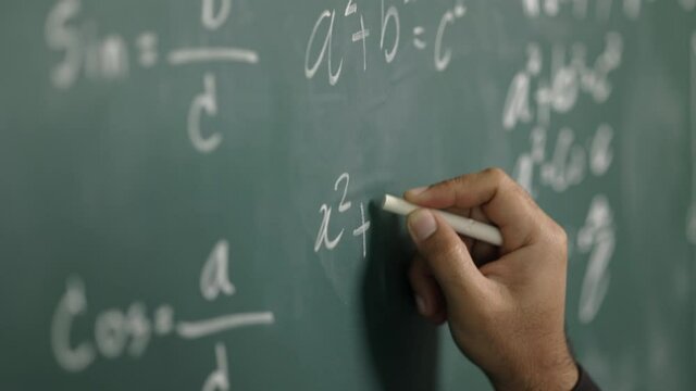 Education background concept. Close up male hand writing mathematical formula on chalkboard.