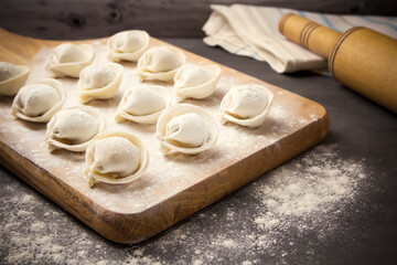 semi-finished pelmeni dumplings on the wooden board.