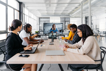 Group of multiracial businesspeople sitting around table having a remote video conference in modern workplace