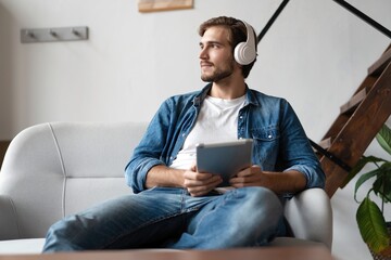 Cheerful young man holding digital tablet and looking relaxed while lying on the couch at home