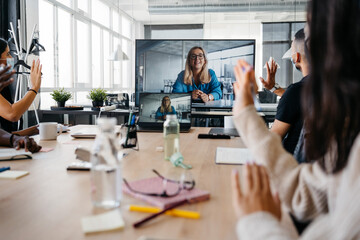 Multiethnic group of workers wearing face masks greeting coworker in a virtual meeting