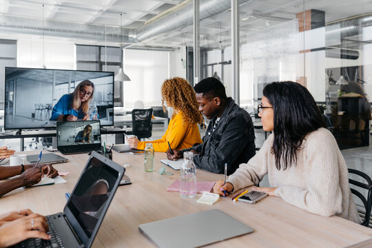 Group of multiracial businesspeople sitting around table having a remote video conference in modern workplace - Powered by Adobe