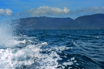 Seawater splash from speed boat, suspended in the air with blue sky and mountain in background.