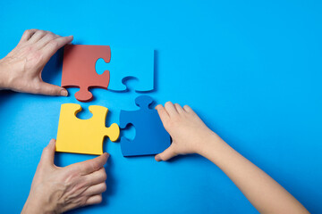 Top view hands of a autistic child and father arranging color puzzle symbol of awareness for autism spectrum disorder. Autism Awareness Day or month.