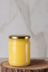 Ghee clarified butter desi in glass jar with rosemary on natural wooden background.