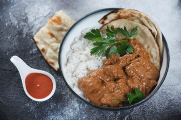 Bowl with indian chicken makhani, white rice and flatbread over dark grey stone background, horizontal shot, elevated view