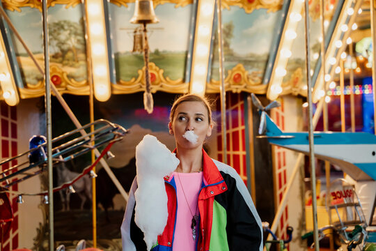 Trendy woman standing in front of fair carousel holding a cotton candy