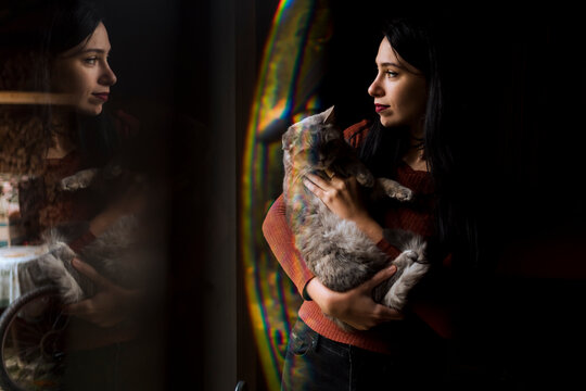 Woman in front of the window with her cute cat, looking outdoor.