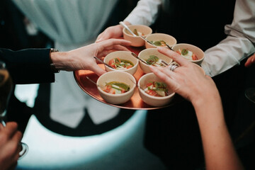 waiter serving appetizer dishes in small ceramic cups to female guests