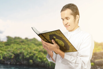 Asian Muslim man standing and reading the Quran