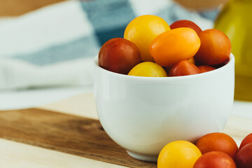 Closeup of various types of cherry tomatoes in a white bowl on a wooden table