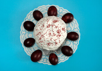 Easter composition. Painted eggs and a glazed Easter cake decorated with sugar sprinkles on a white napkin close-up on a blue background. Happy Easter Holidays. Top view.