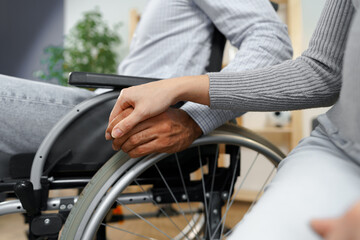 Fototapeta premium Close up of female touching hand of disabled man in wheelchair for support