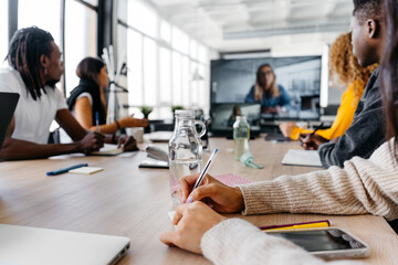 Crop businesswoman writing a note during a remote videocall