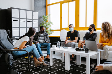 group of diverse coworkers wearing face masks chilling and talking during coffee break in a modern and bright workspace