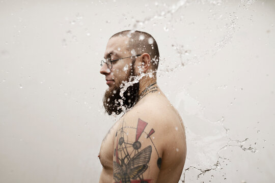 Young man with tattoos stands under a stream of water