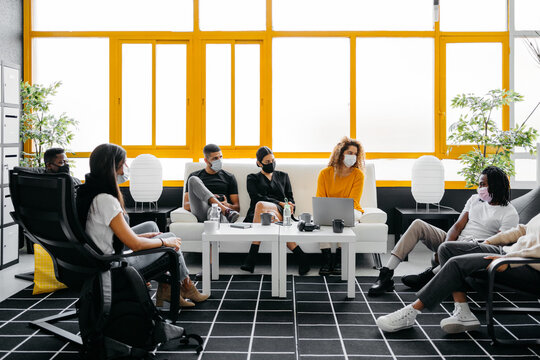 group of diverse coworkers wearing face masks chilling and talking during coffee break in a modern and bright workspace