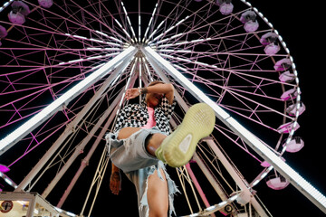 Trendy woman having fun and dancin in a fairground in front of a ferris wheel