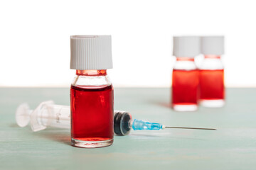 medical vaccine phials with red liquid and syringe over green table and white background. Vaccination and immunization conceptual.