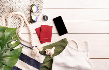 Flat lay travelling objects with swimsuit, smartphone, passports, sunglasses and compass on white wooden background