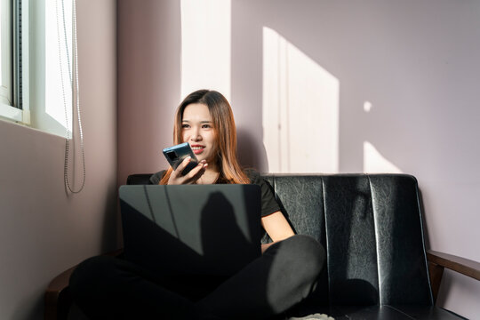 A woman sitting on a sofa in front of the window using a mobile phone