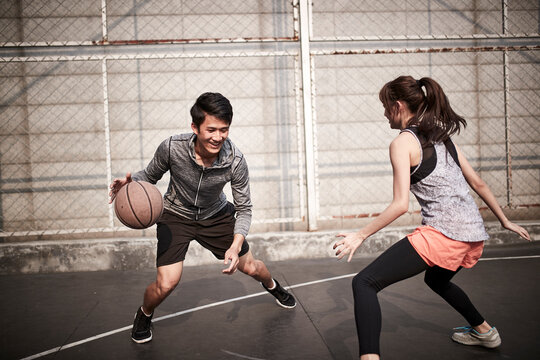 young asian man and woman playing basketball for fun