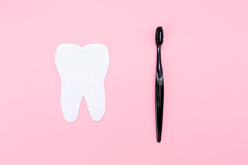 Concept of hygiene of the oral cavity. A toothbrush and a felt-cut out tooth. Flat lay. Pink background. Copy space