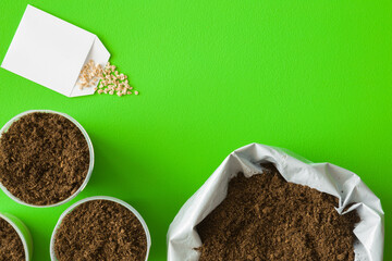 Opened sack and full pots of fresh soil, white paper pack of seeds on green table background....