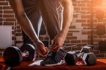 Fototapeta na wymiar Fitness motivation and muscle training concept. Man in sneakers tying shoelaces in sunlight. Athlete starting exercise with dubbell weight.