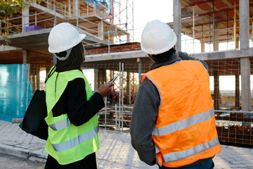 Back of Woman engineer and construction worker checking the development of a building in construcion.