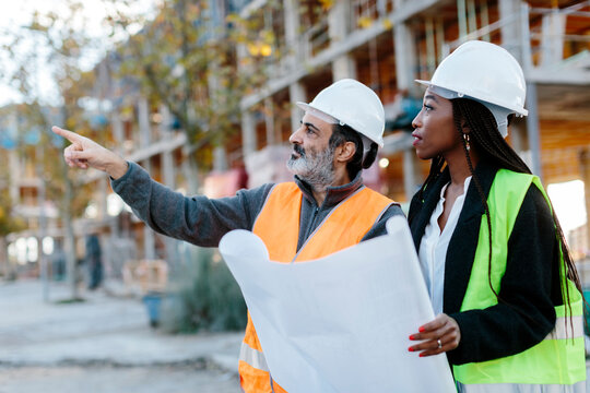 Construction worker reporting to woman engineer while holding some blueprints in front of the construction.