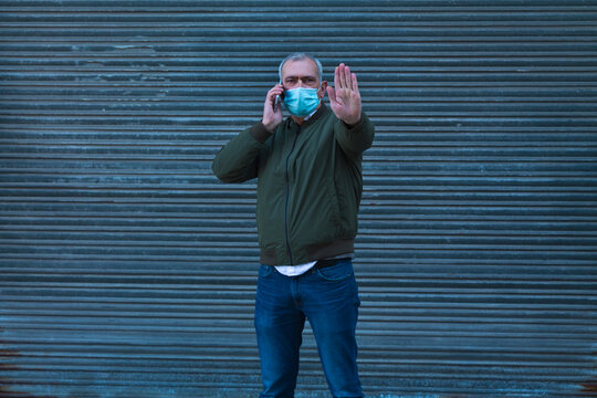 man with medical mask using mobile phone and making stop with hand