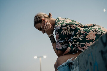 Young stylish woman sitting on top of wall with graffity with pensive face looking down