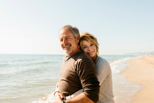 Mature married couple hugging each other standing at the beach